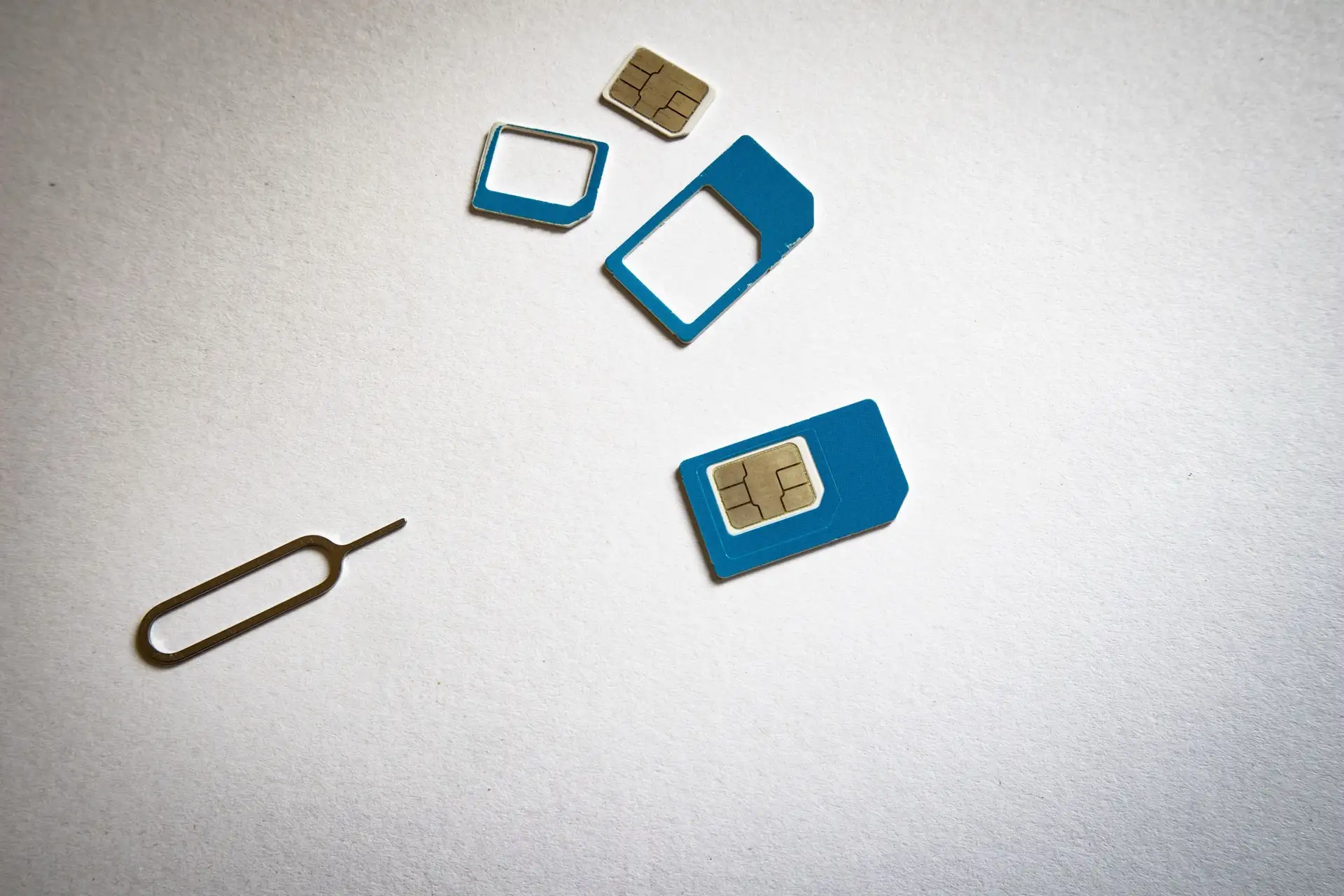 A blue nano SIM card with its micro and mini adapter frames and a metal ejector pin, laid out on white paper.