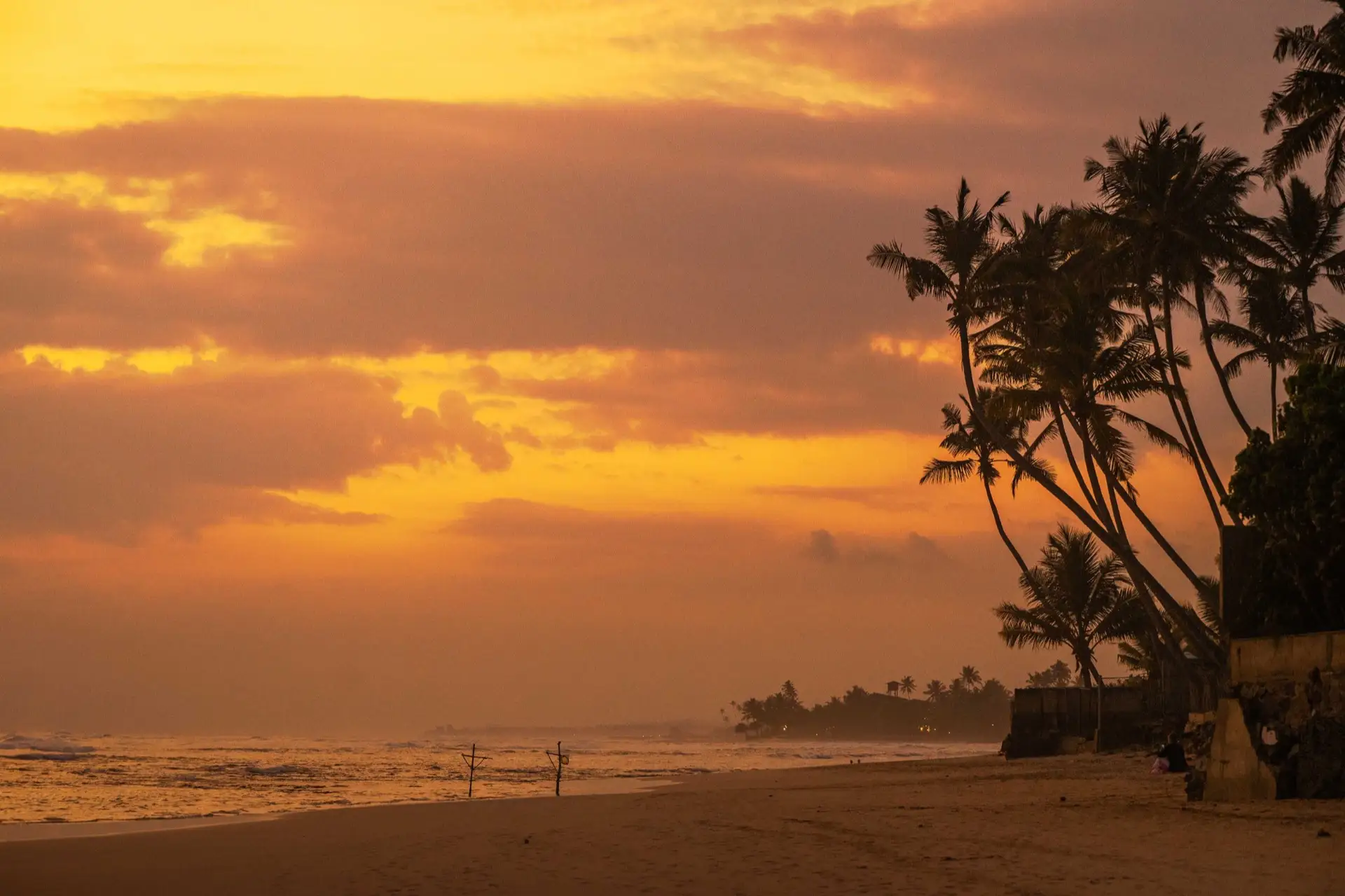 A sandy beach at Ahangama on Sri Lanka's south coast, with surf breaking over a low reef and coconut palms along the shoreline.