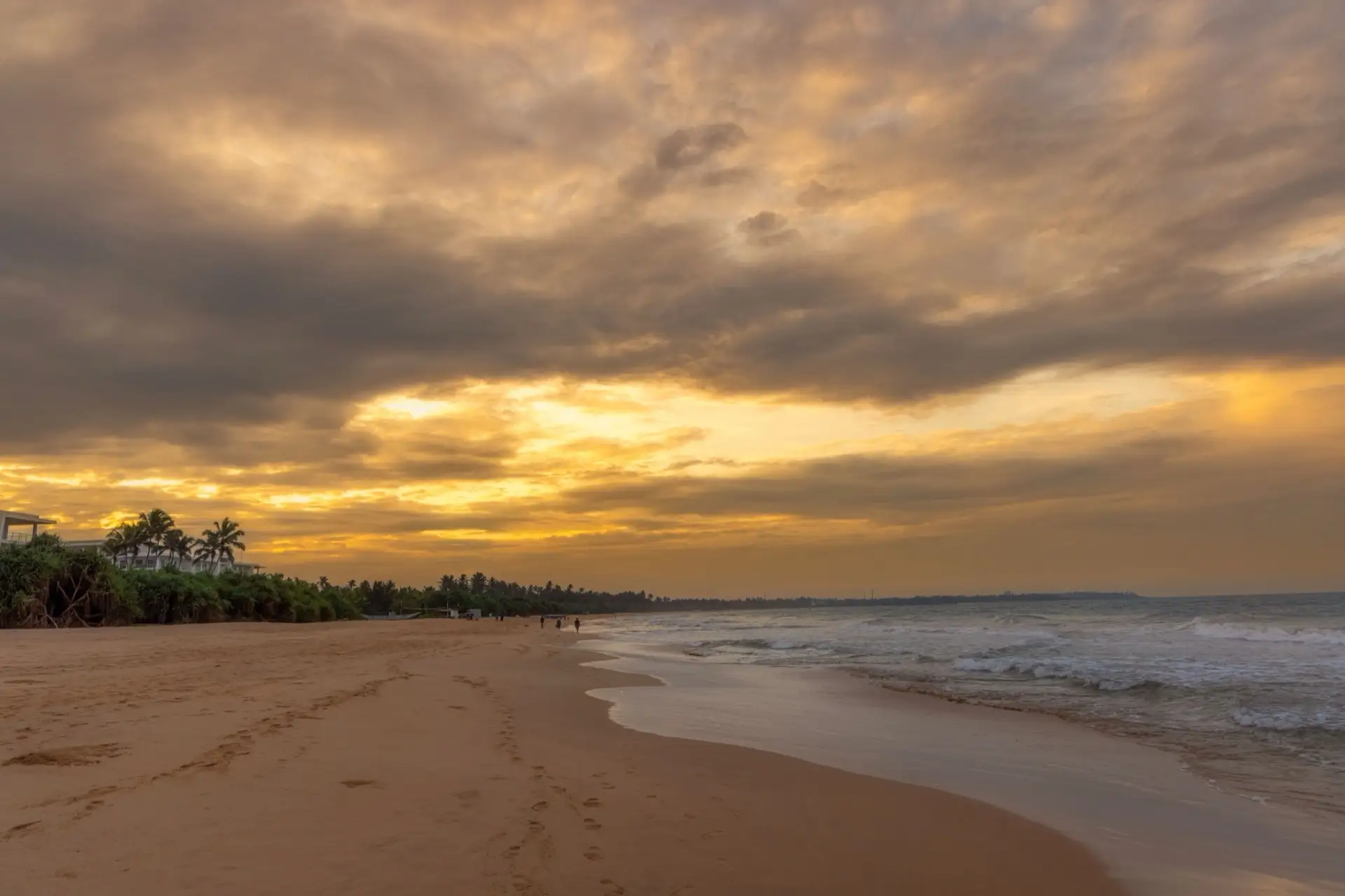 Wide empty sand running into the distance at Bentota beach under a heavy gold sunset.