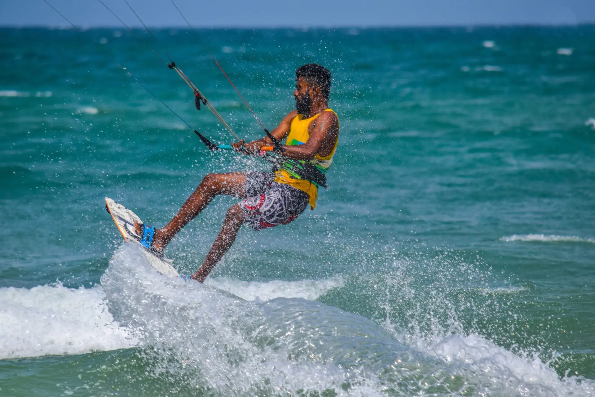 A kitesurfer in a yellow vest carving through turquoise open water off Kalpitiya, throwing up a wall of spray, with the kite lines running out of the frame.