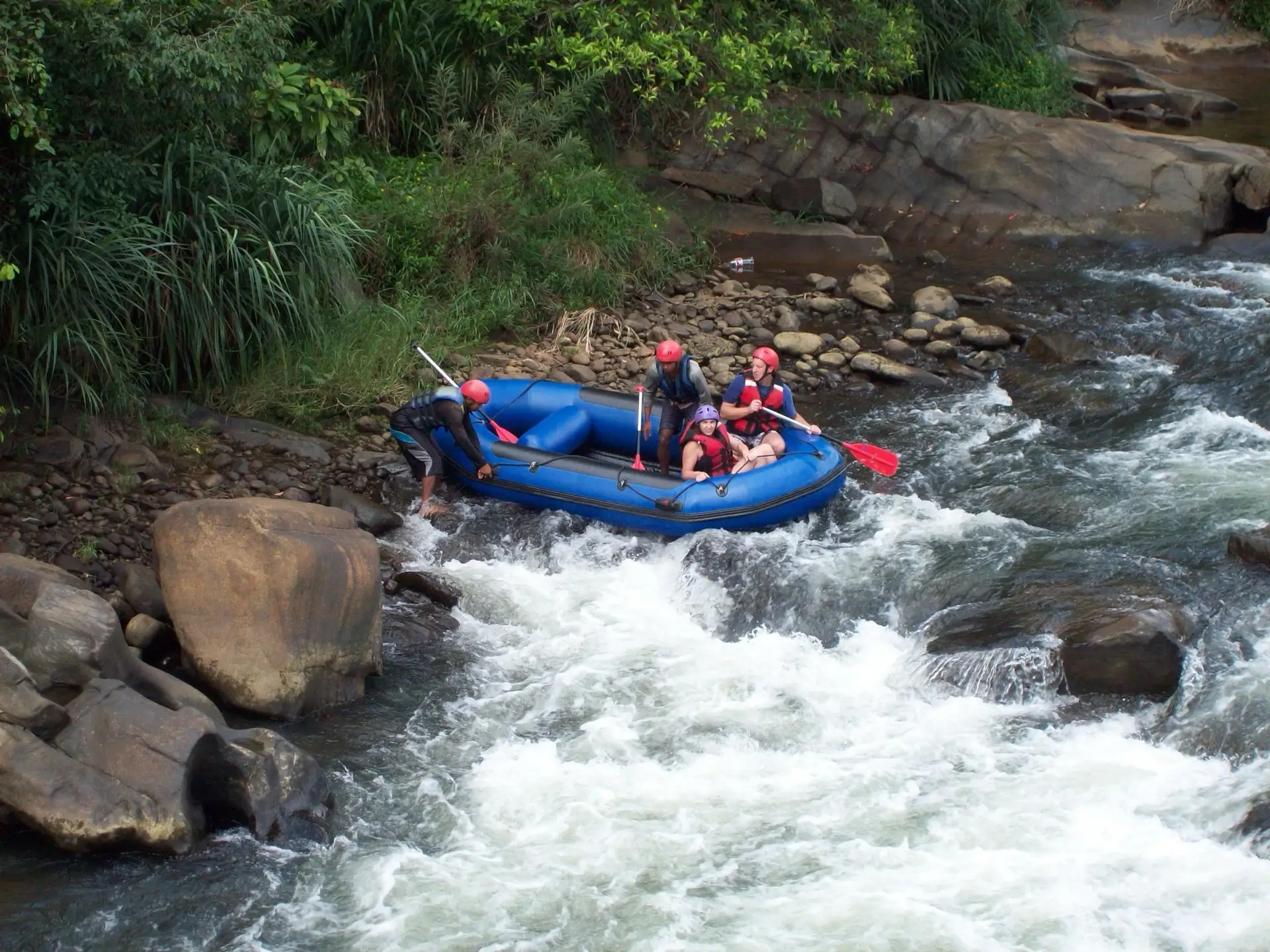 The wide Kelani river running between forested hills at Kitulgala, with rapids breaking over rock in the foreground.