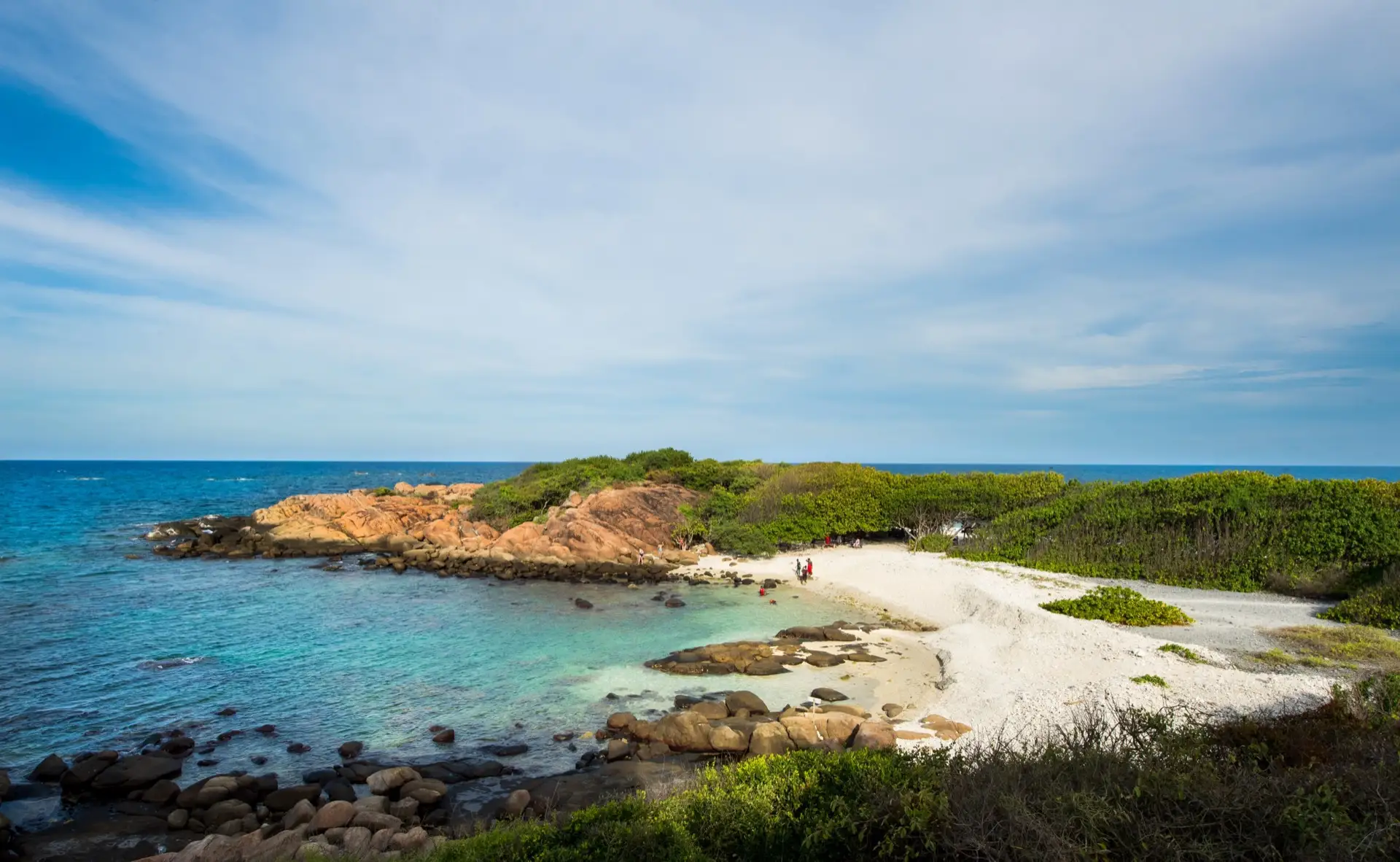 A wide flat stretch of pale sand at Nilaveli with shallow blue water running up the beach and coconut palms behind it.