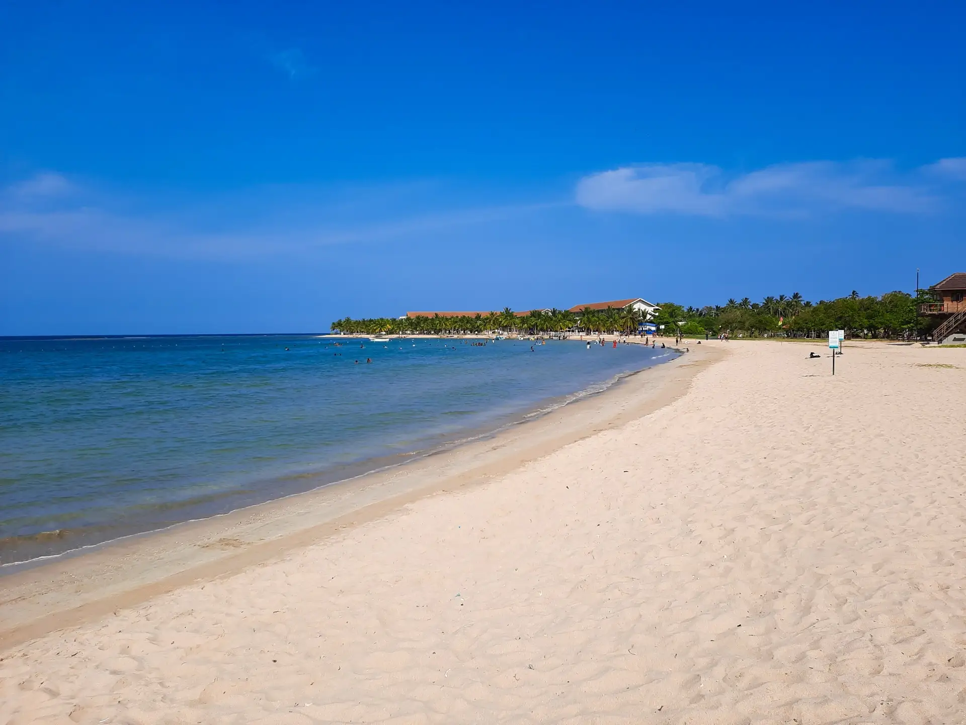 A calm shallow bay at Pasikuda with pale sand curving round to a low headland and a line of palms behind the beach.