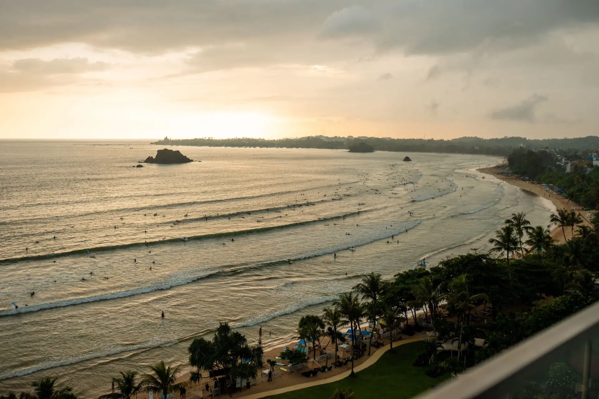 The wide crescent of Weligama Bay on Sri Lanka's south coast, with surfers in the shallows and coconut palms along the shore.
